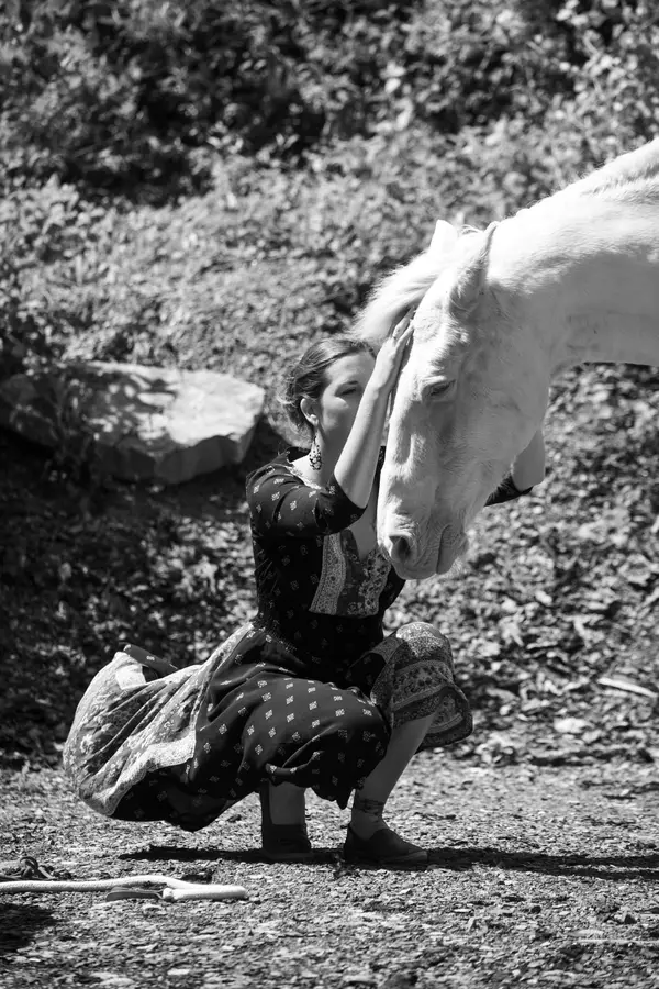 Amélie Ballif Berclaz accroupie, la main posée sur le front d’un cheval blanc.
