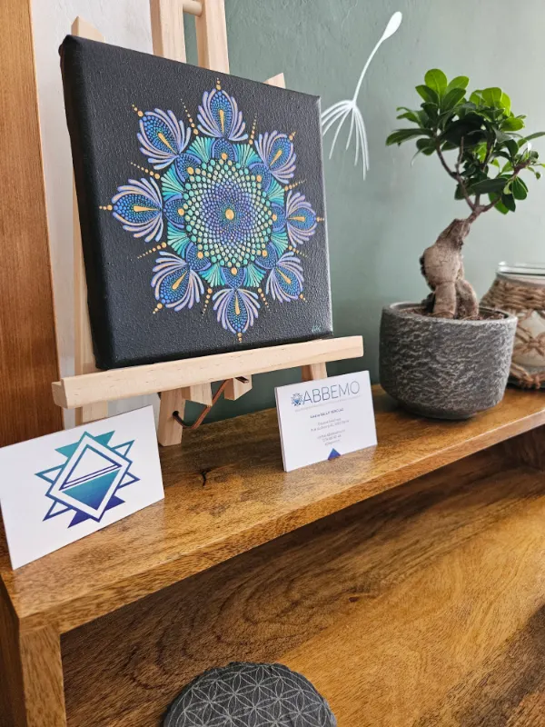 Un mandala peint à la main sur un chevalet, un bonsaï et les cartes Abbemo, sur le bureau du cabinet.